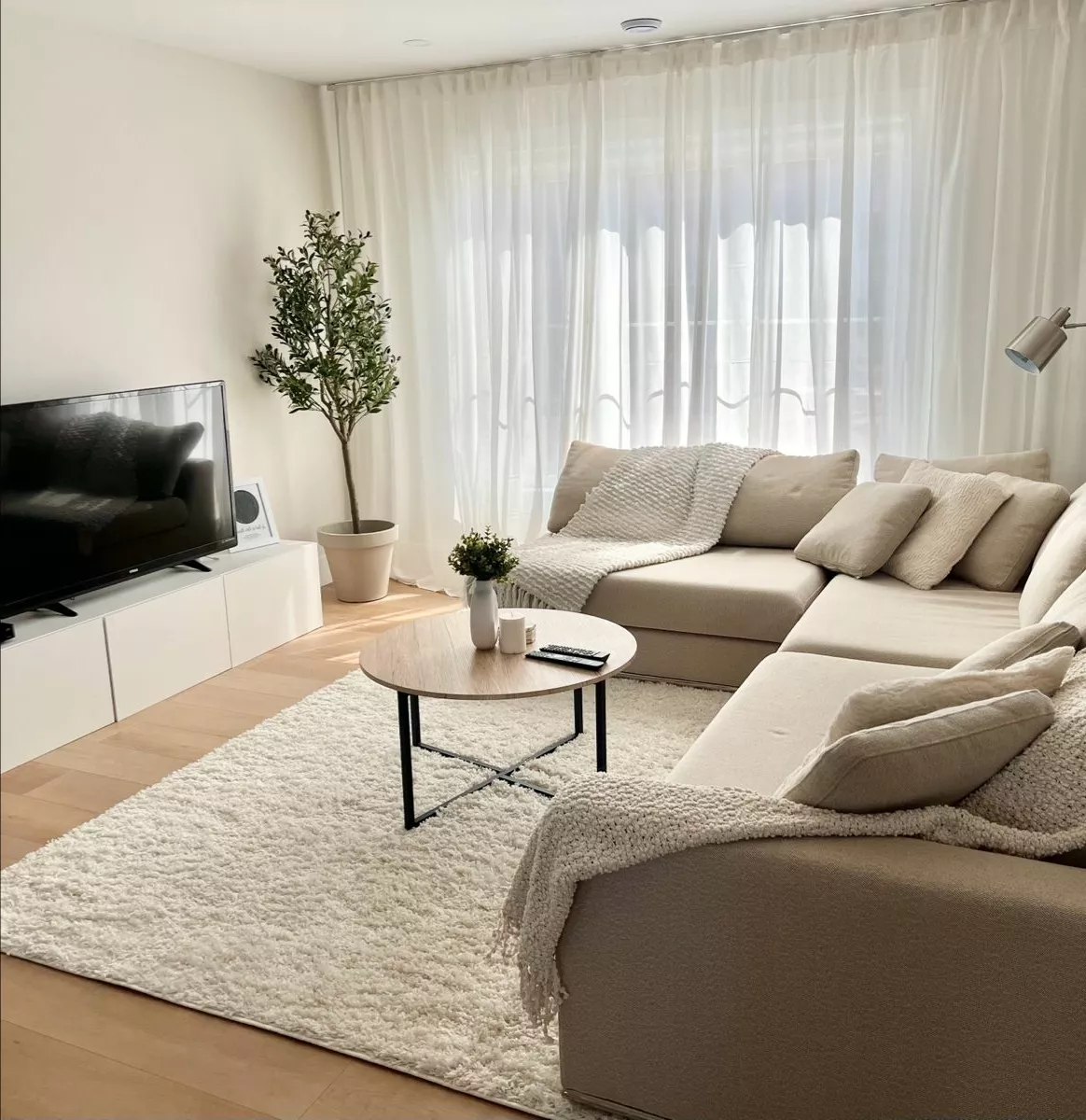 Explore this tranquil living room featuring elegant off-white decor, a cozy L-shaped sofa, and minimalistic furnishings for a serene and stylish space.