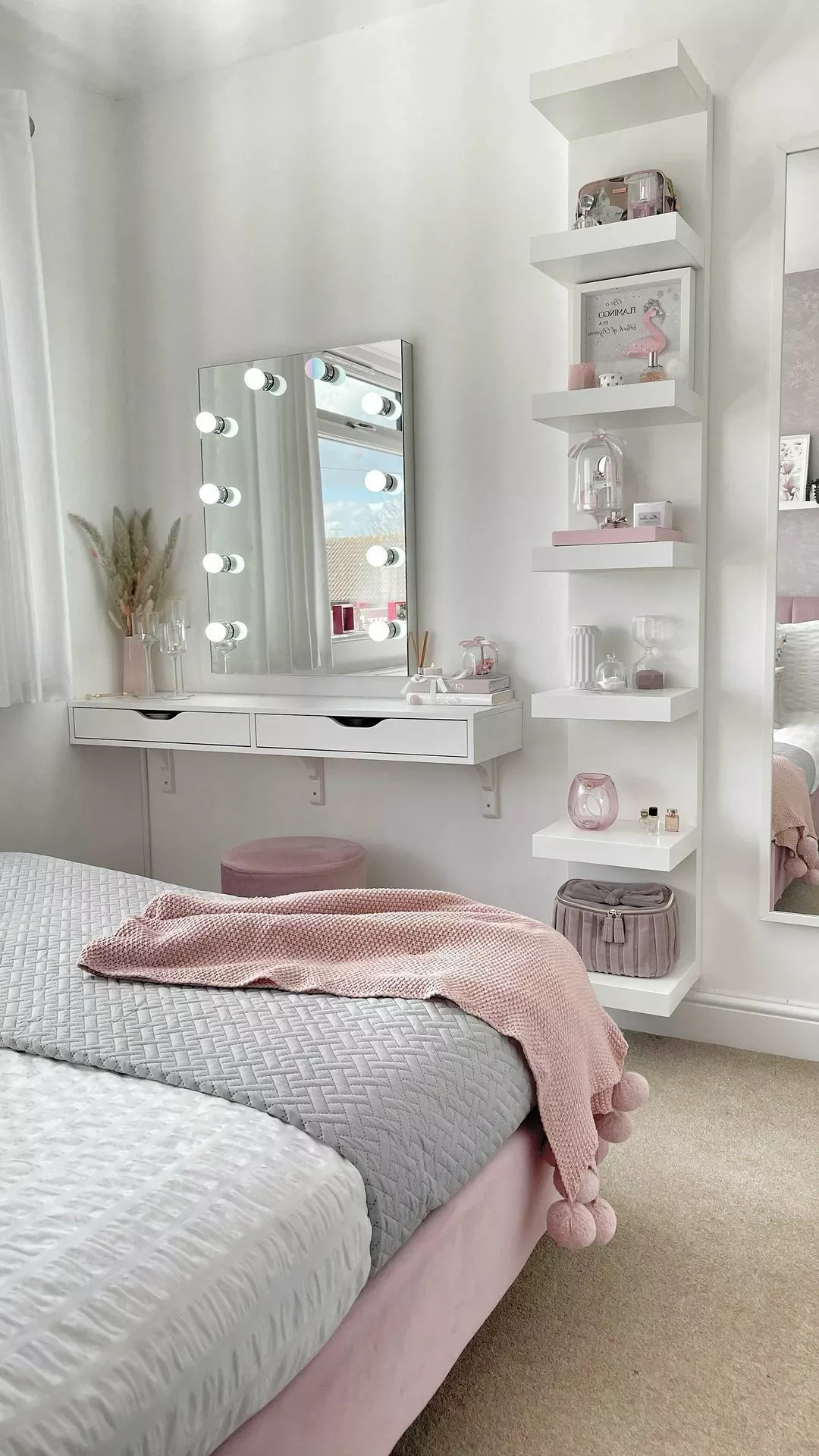 Discover a stylish vanity setup complete with a well-lit mirror, floating shelves, and pastel decor that elevates any bedroom space.