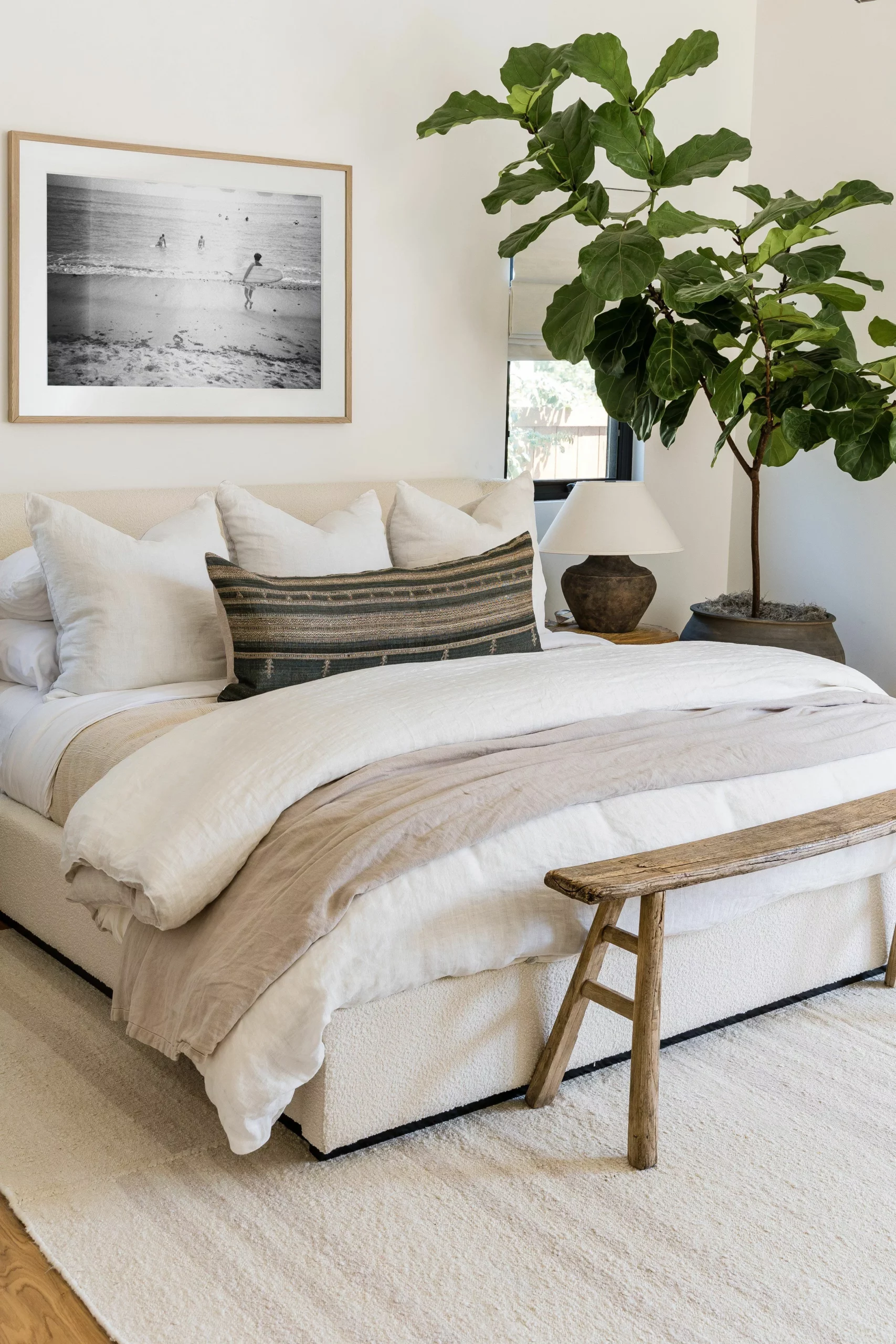 Discover the perfect blend of comfort and design in this stylish bedroom featuring a plush bed, rustic bench, and a touch of nature with indoor plants.