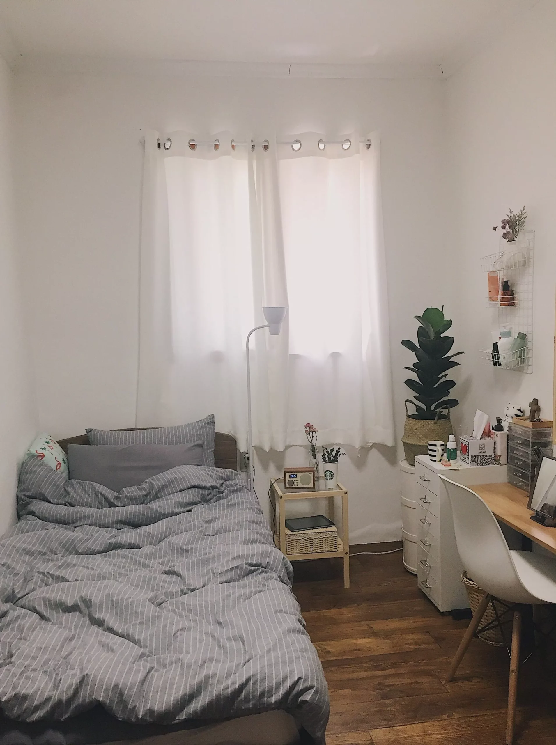 Discover the tranquility of a minimalist bedroom featuring airy curtains, a comfy bed, and a stylish work corner.