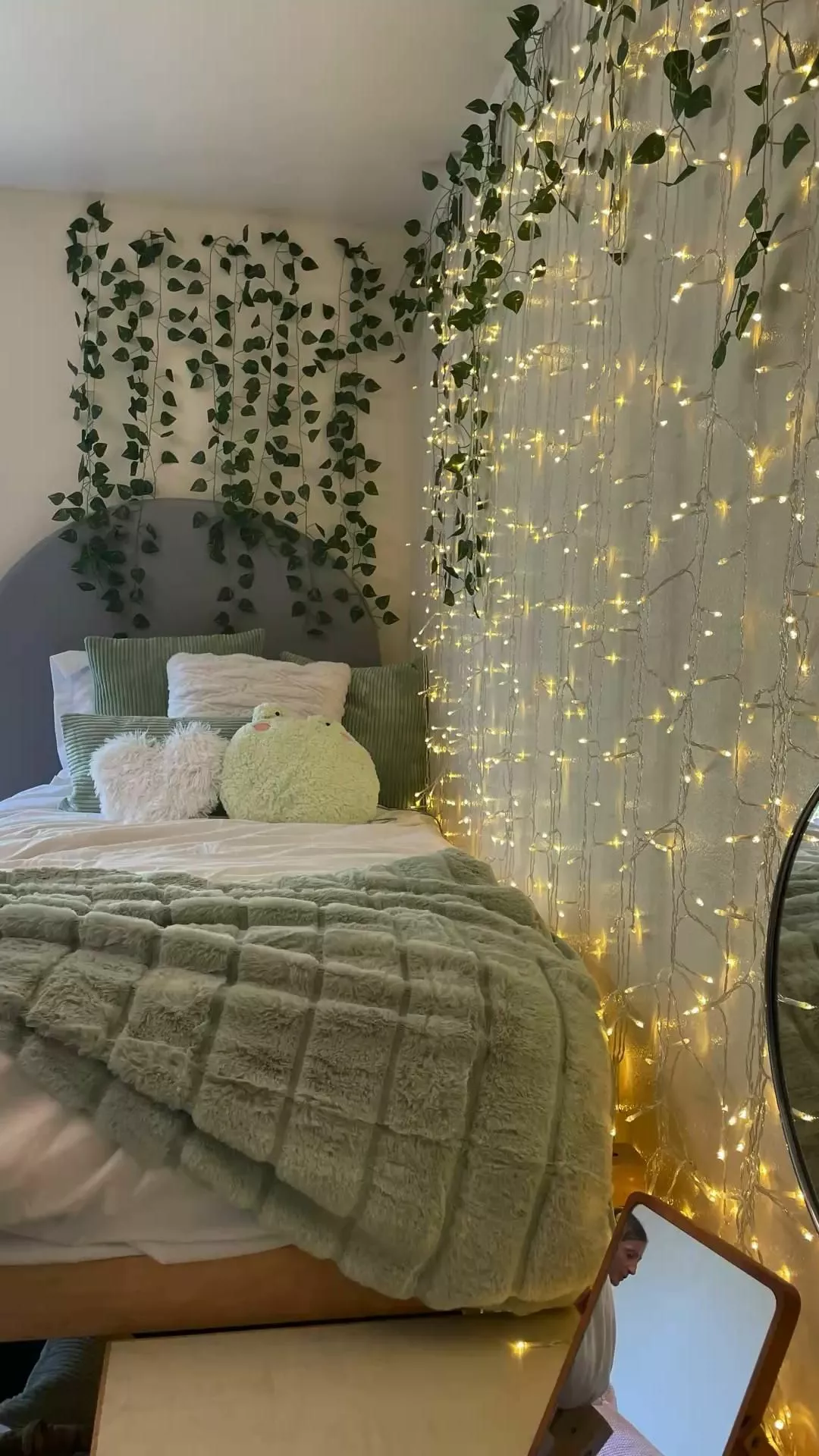 Discover the serene and magical ambiance of this bedroom, adorned with lush green decor and twinkling fairy lights.