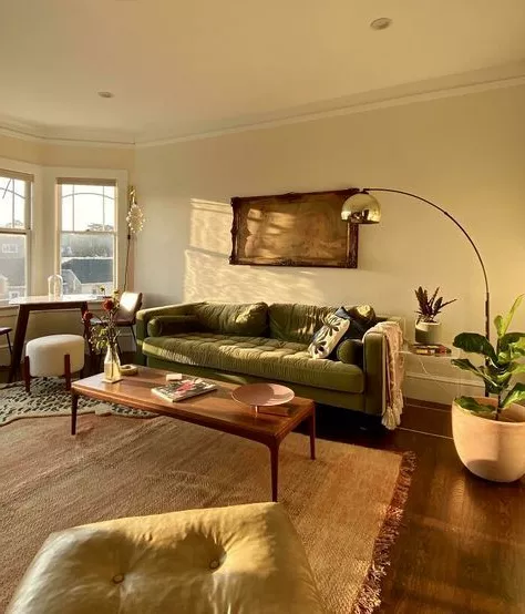 Discover the perfect blend of modern and vintage aesthetics in this sunlit living room featuring a plush green sofa and elegant wooden furniture.